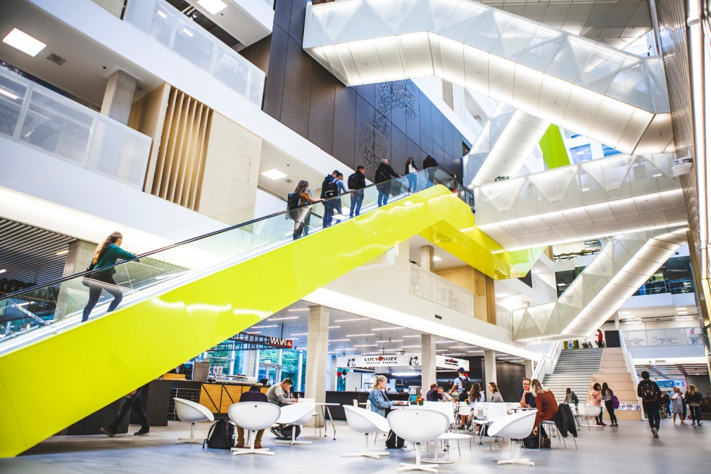 Das Bild zeigt eine moderne gläserne Halle mit Tischen und vielen Treppen am HU Campus in der Heidelberglaan