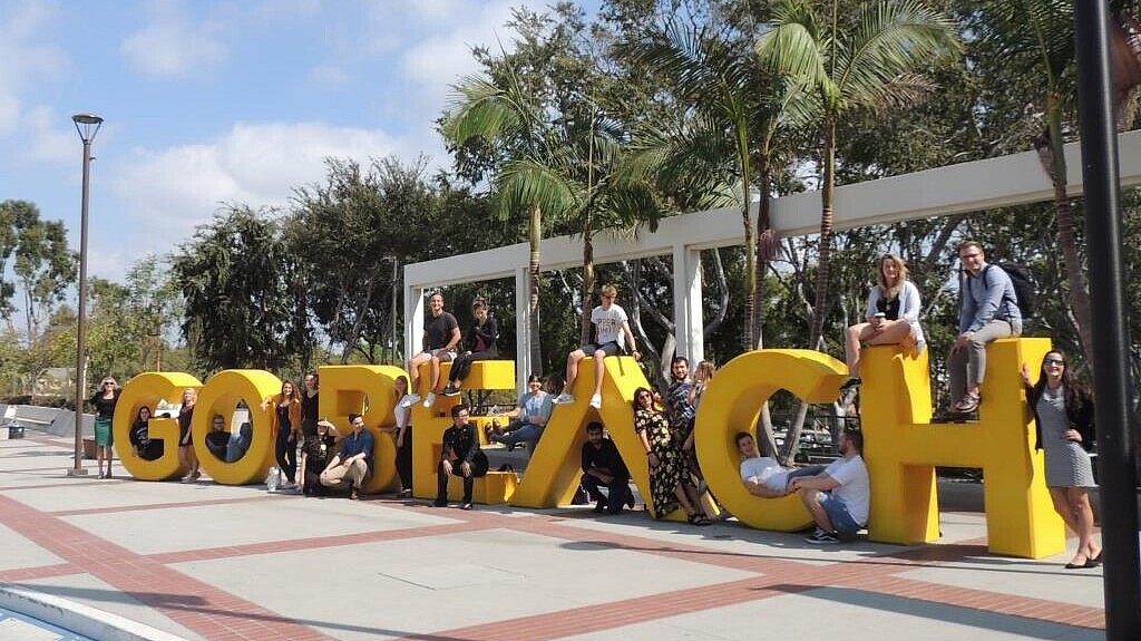 Group of students sitting on large letters that spell Go Beach